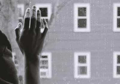 A woman's hand resting against a windowpane suggests grief. In counselling, the dual process model of grief states that both denying and avoiding are important parts of a healthy grieving process.