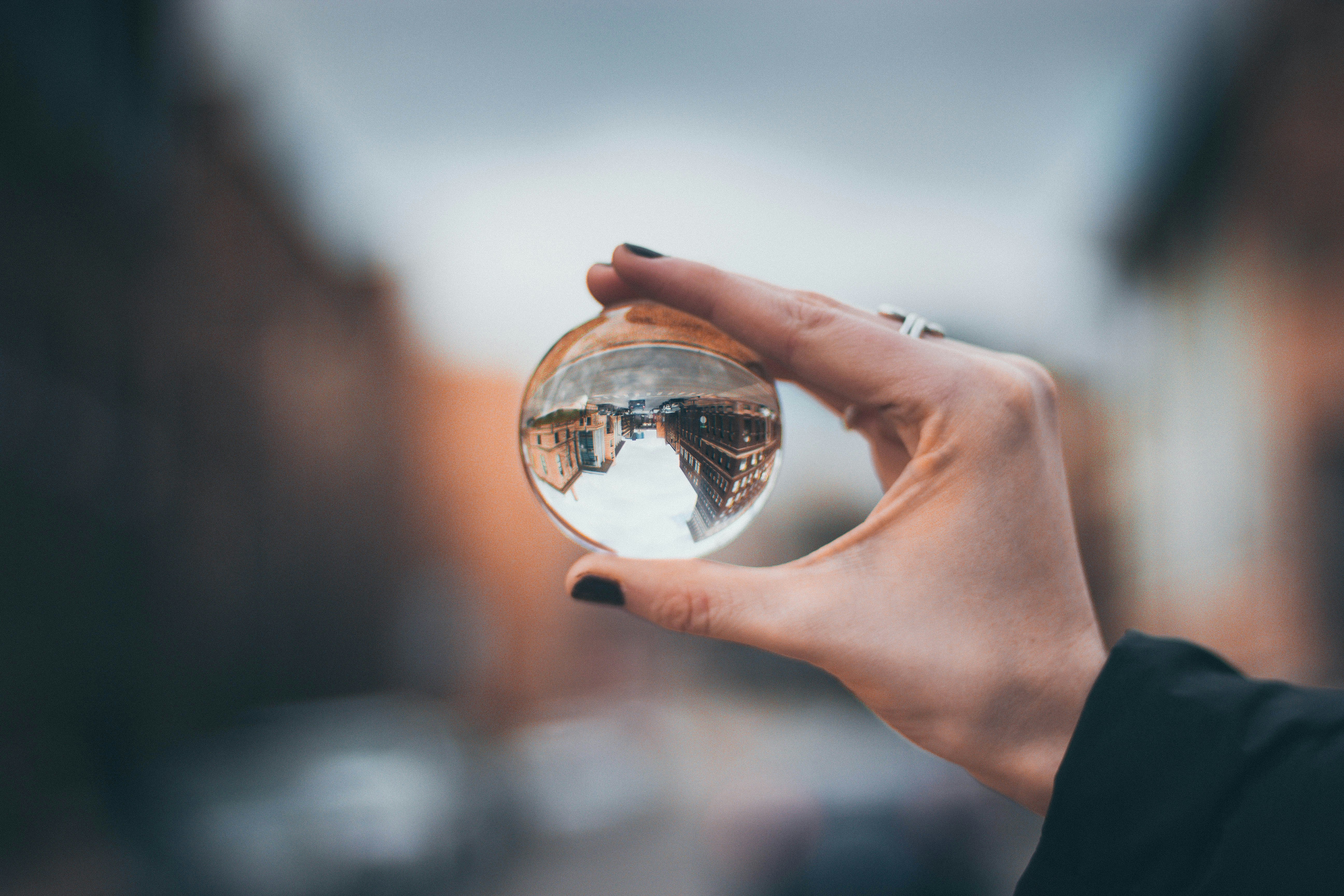 A hand holds a transparent glass sphere. The background is blurred with only the view of buildings seen through the glass sphere is clear. This image represents seeing trauma clearly making sure we understand the definitions of trauma.